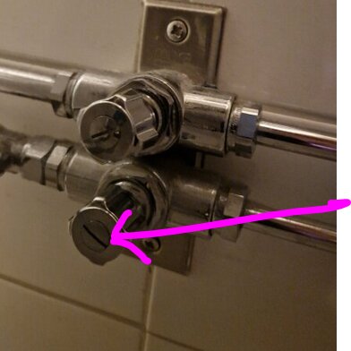 Duschreglage med rör, en rosa pil pekar på undre kranen. Metall, väggfäst, funktionell design.