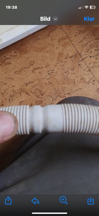 Ett handtaget flexibelt rör eller slang framför en korkgolvbakgrund hålls av en person.