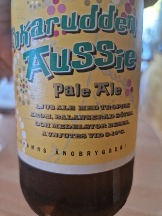 Flaska av 'Aussie Pale Ale' med färgglad etikett från Tjärnaruddens Ångbryggeri, bryggd med tropisk arom.