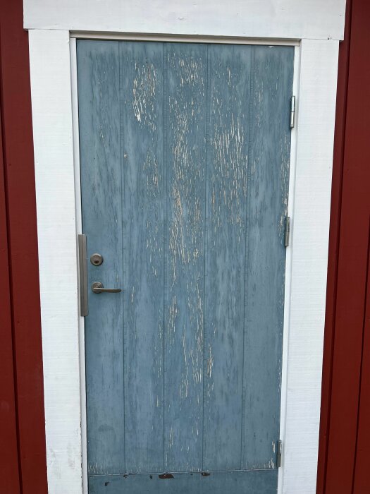 Sliten blå dörr med flagande färg, vit karm, röd vägg, handtag och lås.