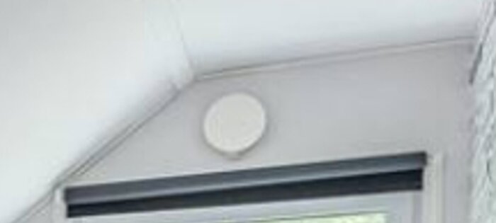 Vitt rum, larmdetektor på taket, fönster med persienn, minimalistisk design.