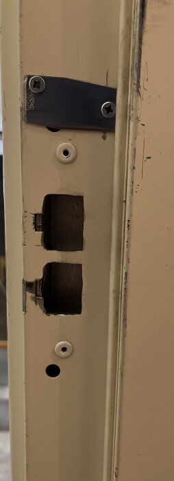 Närbild av slitna detaljer på en dörrkarm med låskista och gångjärnsbeslag.