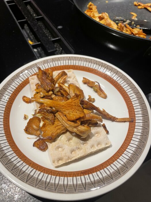 Knäckebröd med stekt svamp på tallrik, stekpanna i bakgrunden på köksbänk.