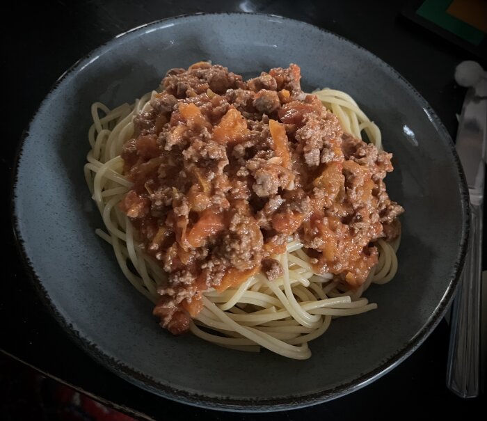 En tallrik spaghetti med köttfärssås, serverad på mörk tallrik, inomhusmiljö, maträtt i närbild.
