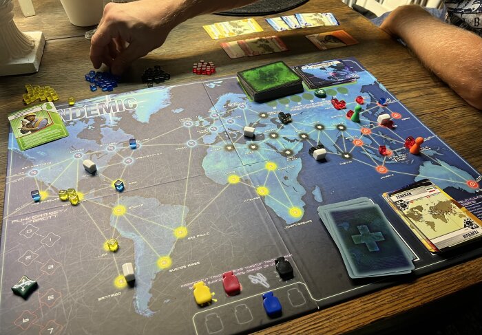 Person spelar brädspelet Pandemic. Spelplan, kort, pjäser som representerar sjukdomar och botande aktiviteter syns.