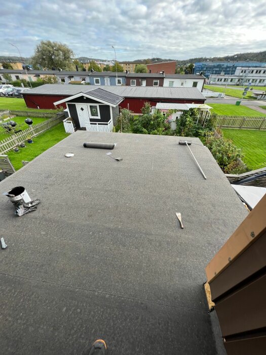 Tak med verktyg och material, utsikt över trädgårdar och hus, molnig himmel, personens sko syns.