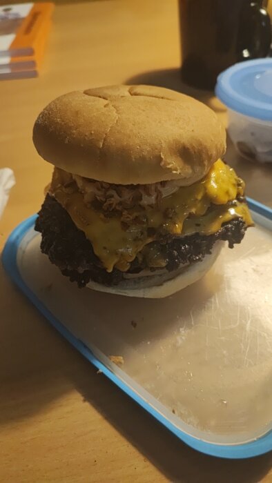 En hamburgare med bröd, ost, väl tillagad biff på ett blått fat. Bakgrund oskarp, närbild.