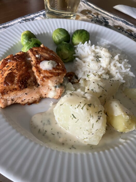 Laxfilé, kokt potatis, ris, brysselkål på tallrik, vit sås, dill, matplats.