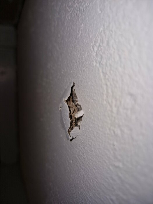 Vit vägg med skada; ytskiktet är bortskrapat och exponerar underliggande material.