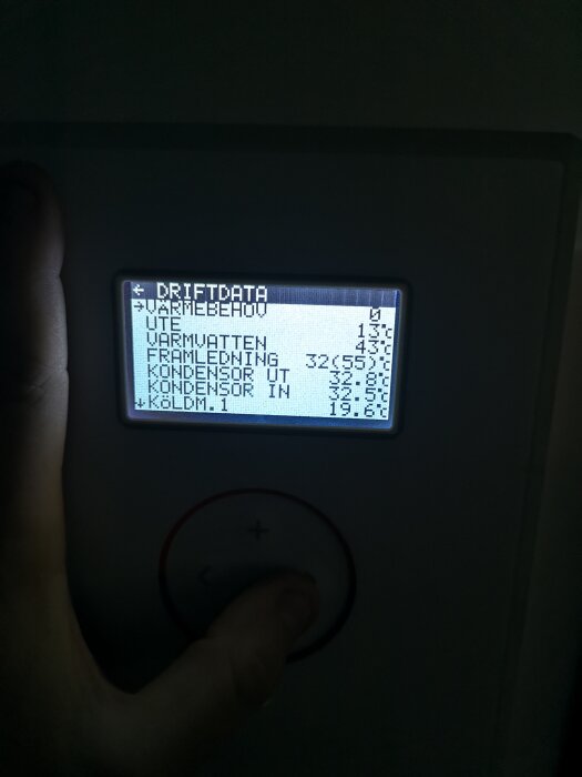 LCD-panel som visar driftdata för värmesystem, hand justerar inställningar via knappsats.