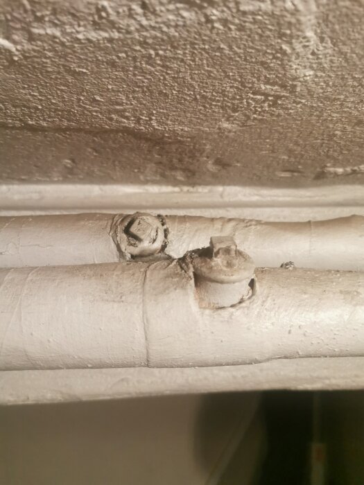 Isolerade rör och fittings med klämmor på en ojämn vägg, antyder möjligtvis äldre VVS-installation eller underhåll.