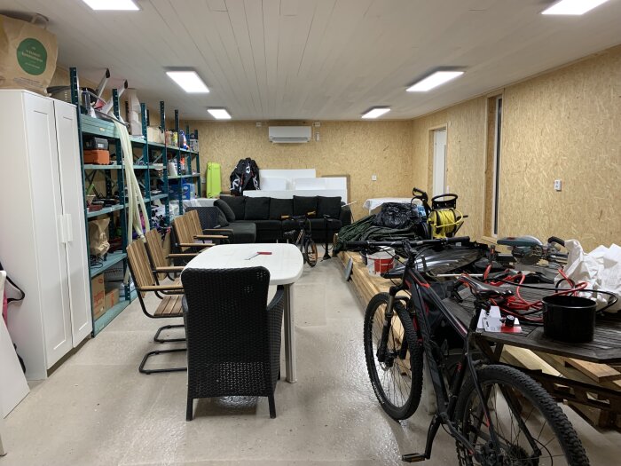 Ett rörigt garage med cyklar, möbler, hyllor och diverse föremål.