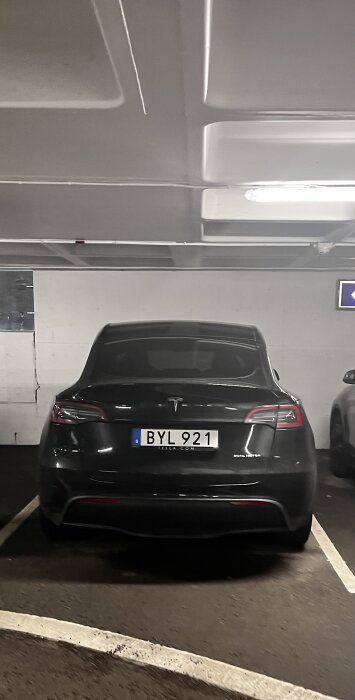 En parkerad Tesla Model 3 i ett garage, belysning ovanifrån, registreringsskylt synlig, rent och organiserat utrymme.