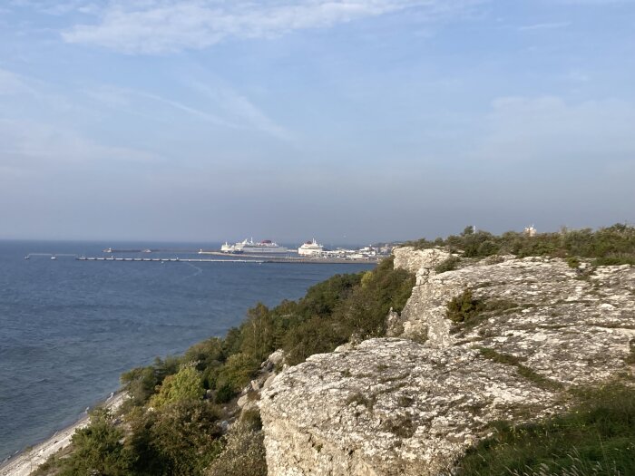 Klippiga kusten, utsikt över hamn med kryssningsskepp, lugnt hav, delvis molnig himmel.