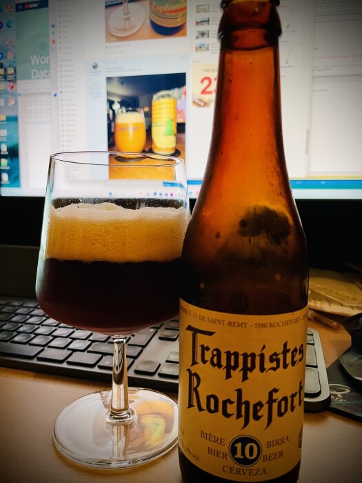 Ölglas och flaska framför datorskärm, Trappistes Rochefort, tangentbord, arbetsstation, fokus på öl.