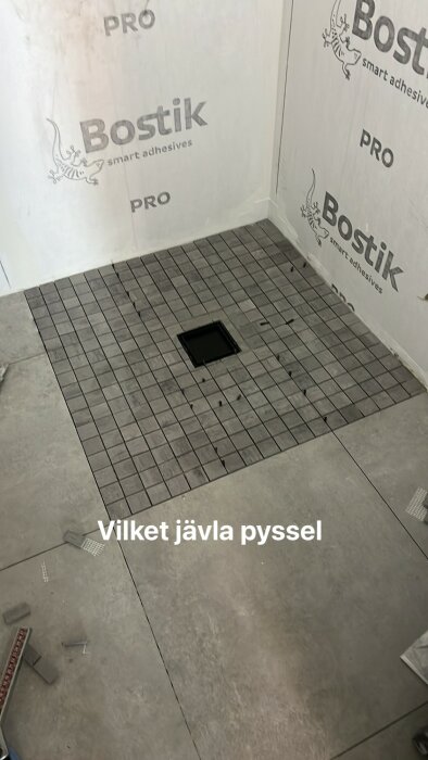 Kakelarbete i ett badrum, delvis lagt golv med mittbrunn, väggisolering, verktyg och text som uttrycker frustration.