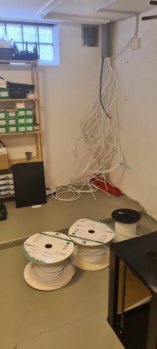 Rörigt kontorsrum med okopplade Ethernet-kablar, hyllor, serverrack och kabeltrummor på golvet.