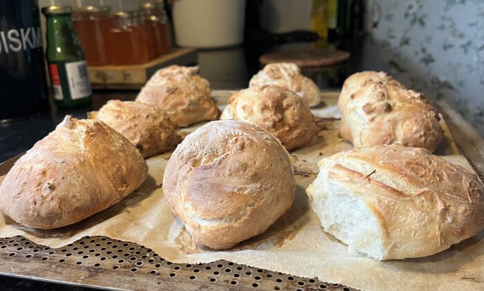 Nybakt bröd på bakplåt, rustikt utseende, köksmiljö, bakpapper, oskarp bakgrund med köksartiklar.