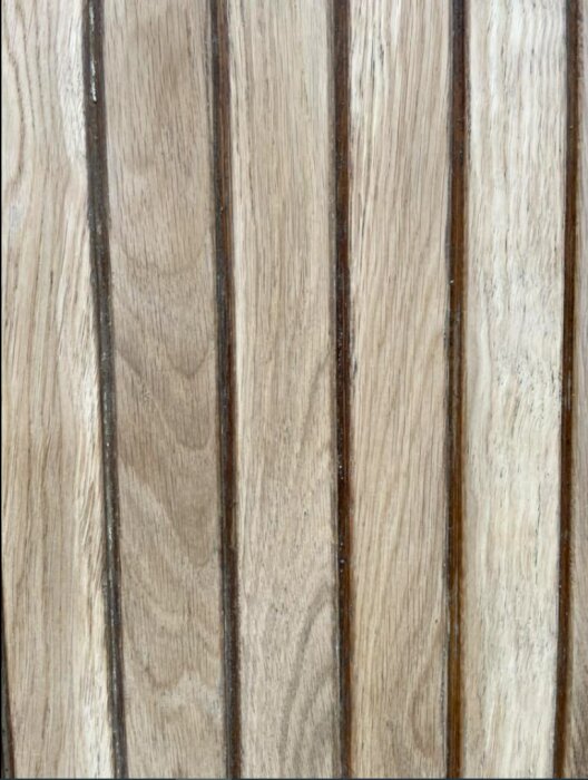 Träpanel med vertikala linjer och synlig träådring. Naturlig, varierande, ljusbrun ton. Strukturerad, dekorativ yta.
