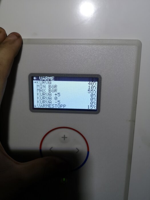 En hand trycker på en digital termostat med temperaturinställningar och en upplyst display.