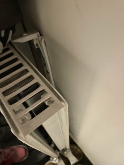 Vit radiator vid en vägg, otydlig bild, del av en sko syns.
