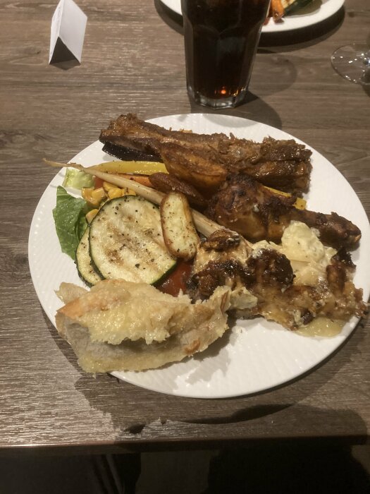 En tallrik med blandad mat inklusive grönsaker, kött, och bröd, på ett bord med dryck.