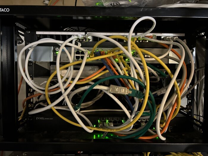 Nätverksskåp med trassliga Ethernet-kablar och nätverksutrustning. Behov av kabelhantering.