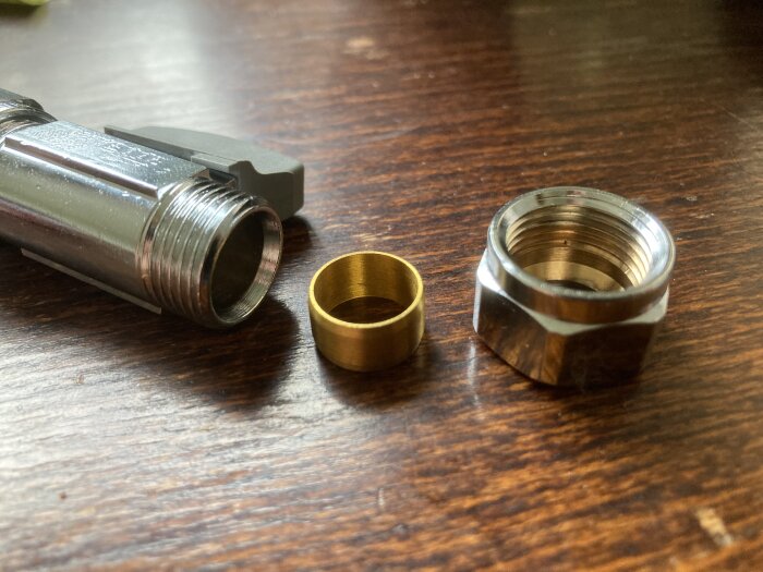 Metalliska rörkopplingsdelar på träyta: munstycke, guldfärgad ring, sexkantig förbindelse. Verktyg eller VVS-komponenter.