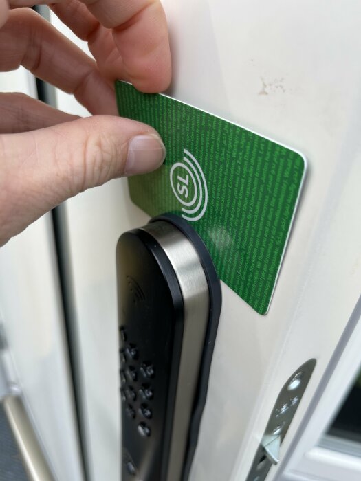 En hand håller ett grönt kort mot en kortläsare för elektronisk tillträdeskontroll.