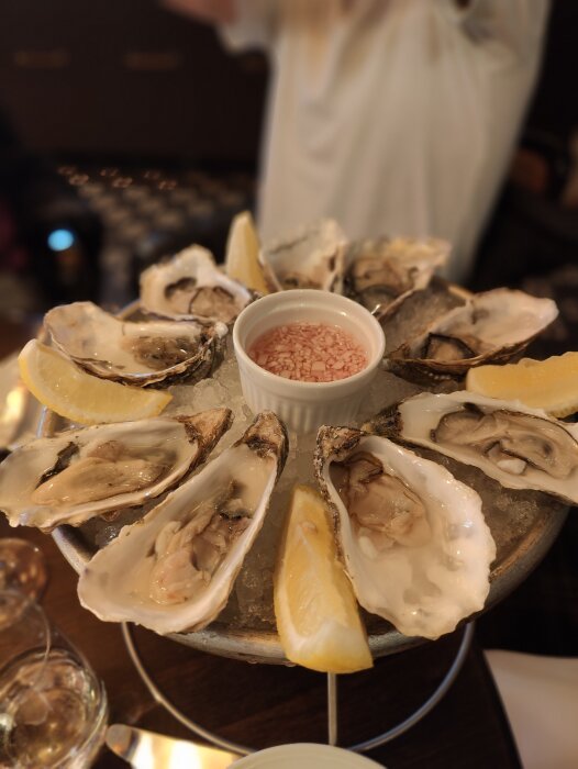 En tallrik med ostron och citron, förgrundsoskärpa, person i bakgrunden, matupplevelse, seafood, färsk.