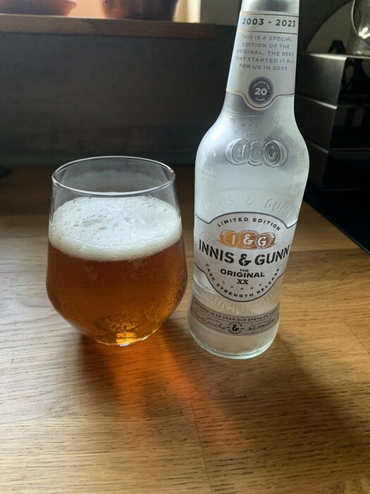 Ett glas med öl och en flaska Innis & Gunn. Limited edition, firar tjugoårsjubileum. Träyta, mysig stämning.