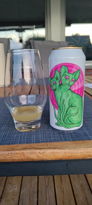 Dryck i genomskinligt glas och burk med kattillustration på trämöblerad utomhusveranda.