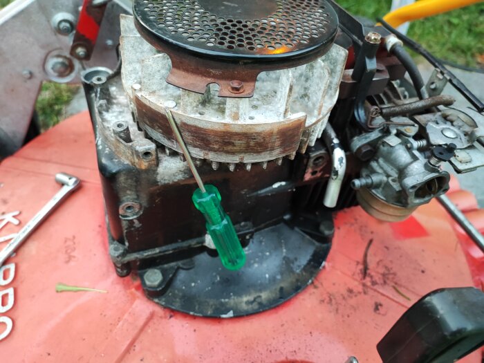 En motor till gräsklippare med skruvmejsel och rost, verktyg på röd yta, underhåll pågår.