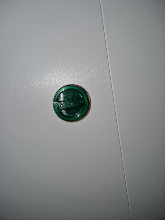 Grön, rund dörrspärr på en vit, vertikal yta med synliga skruvar.