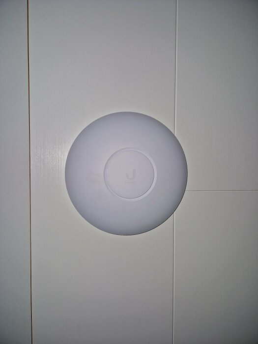 Vit rund takmonterad enhet mot vit vägg vilket kan vara en Wi-Fi-accesspunkt.