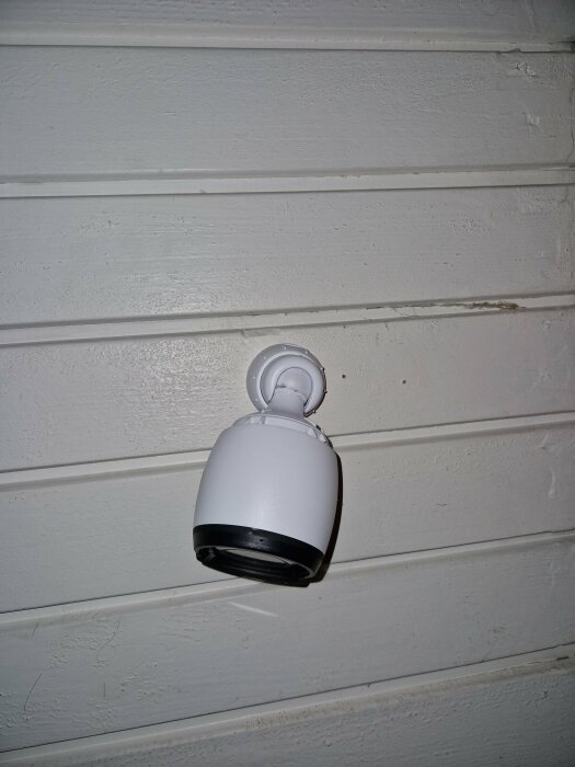 Vit säkerhetskamera monterad på texturerad vit vägg, med övervakningsteknologi.