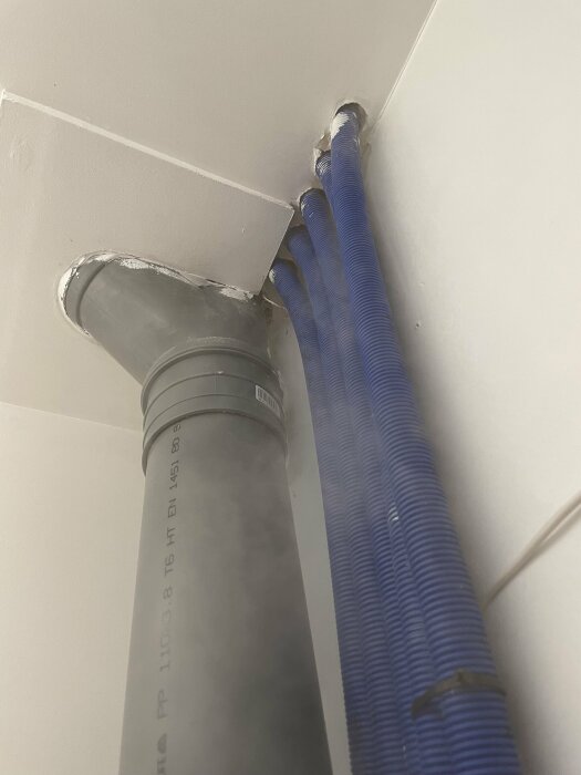 Rörledningar och ventilation går genom taket, täckt med skyddande flexibla hylsor, nära väggens hörn.