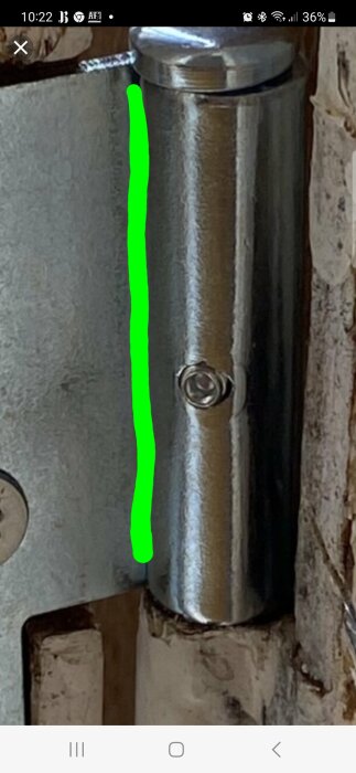 Metallisk dörrhängare eller gångjärn på en dörrkarm, med grön markering längs ena sidan, närbild, skärmdump från smartphone.