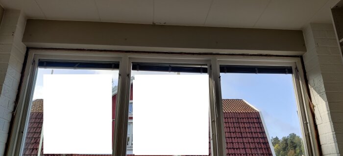 Inomhusvy av tre fönster med persienner och utsikt mot himmel och tak.