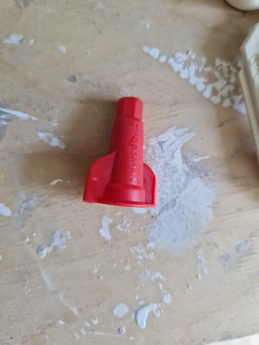 En röd plastskopa på ett skrivbord med mjöl eller pulver runtomkring. Slitage och användning syns på ytan.