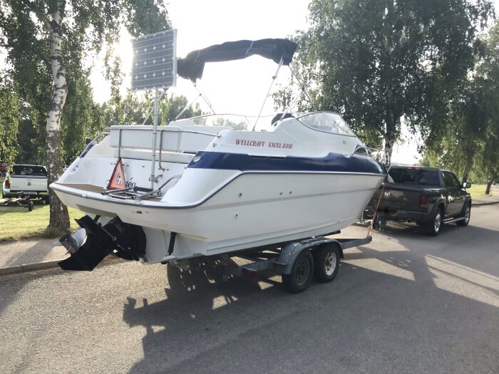 Motorbåt på trailer kopplad till en pickup-truck på en solig parkeringsplats med träd.