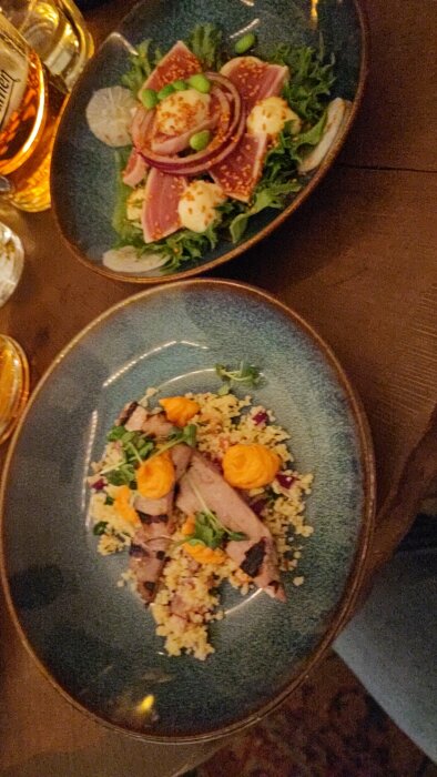 Två maträtter, troligen förrätter, eleganta, couscous, sesamtonfisk, grönsaker, ölglas, otydlig inomhusmiljö, mysig belysning.