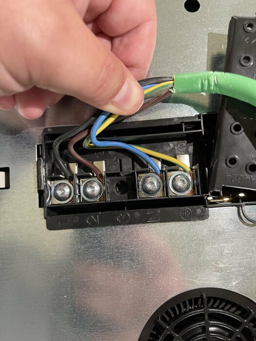 En hand håller elektriska kablar medan de ansluts till en vägguttagets anslutningsplintar. Skruv, säkerhet, elektriskt arbete.