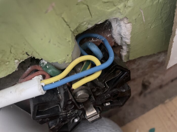 Öppen eluttaget, osäkert, kablar anslutna, byggkaos, behov av elektriker, potentiell fara, väggrenovering pågår.