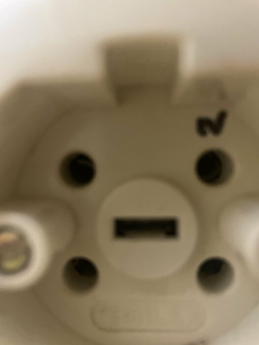 Osammanhängande närbild på en oskarp vit plastartefakt med cirkulära öppningar och en märkning.