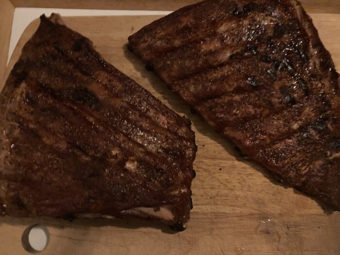 Två grillade köttstycken på ett träskärbräde. Verkar vara saftiga och välkryddade.