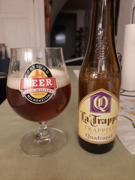 Ett glas mörkt öl och en La Trappe Trappist Quadrupel flaska på ett bord.
