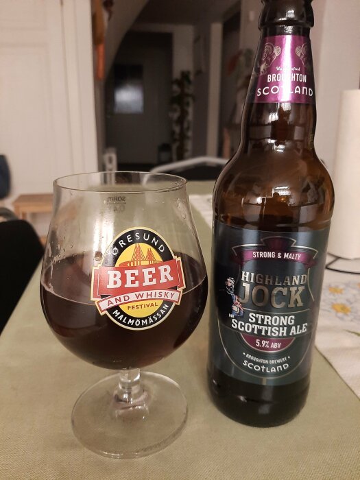 Ett glas öl bredvid en flaska "Highland Jock Strong Scottish Ale" på ett bord.