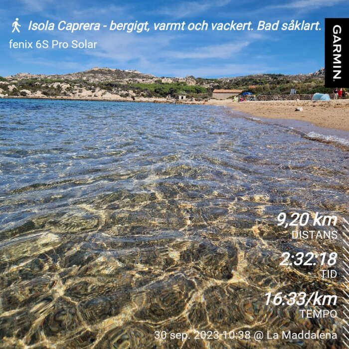 Strandvy, klart vatten, berg i bakgrunden, soligt, skärmdump från Garmin-enhet med aktivitetsdata.