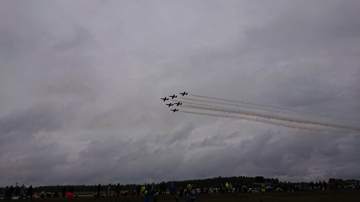 Flyguppvisning, formation, åskådare, mörka moln, rökspår.